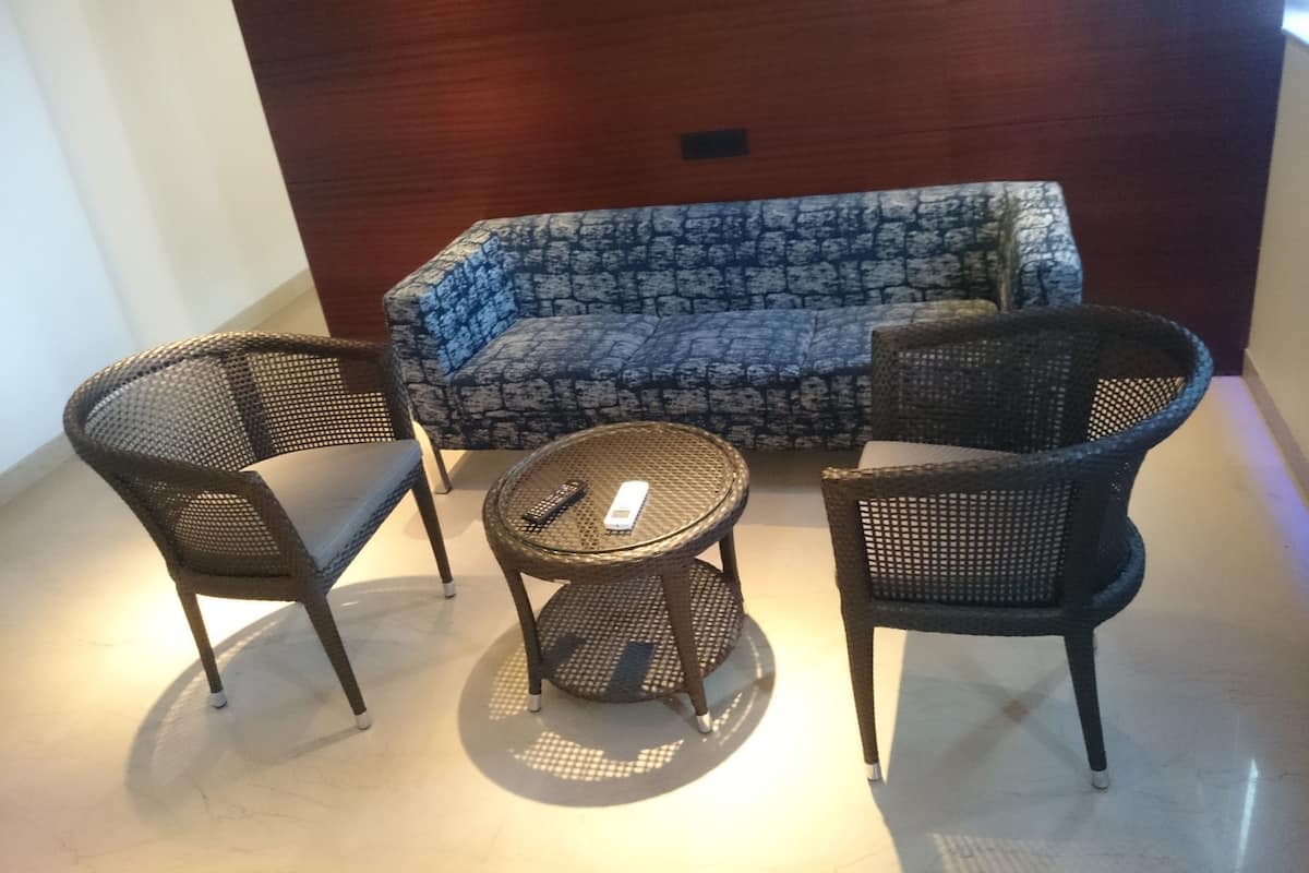 Un área de estar con un sofá estampado, dos sillones de mimbre y una mesita redonda con un control remoto.
