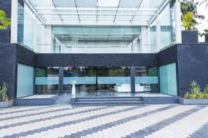 A modern building with a glass entrance, a tiled walkway, and potted plants. - Diana Heights (Aluva)