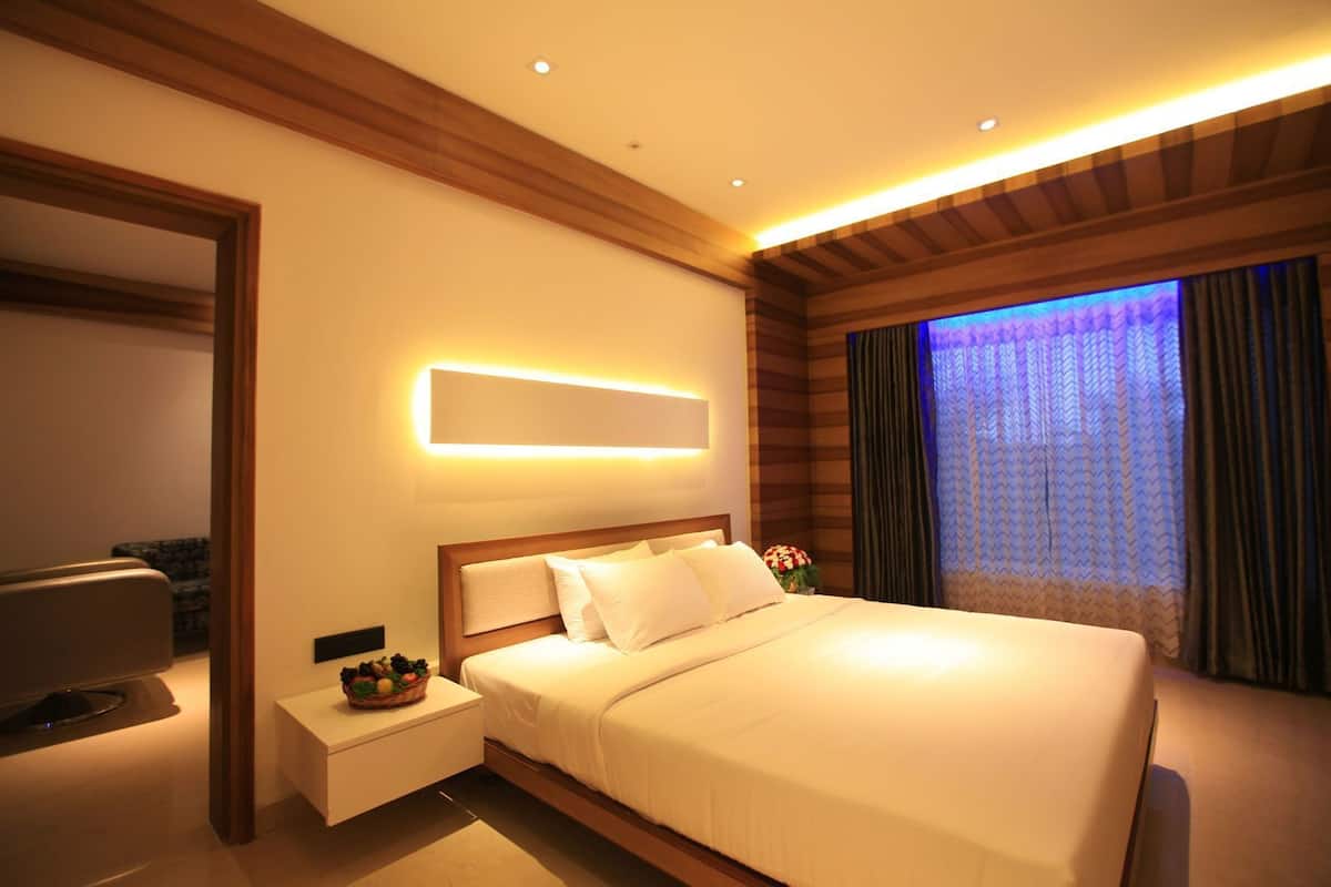 Una habitación de hotel moderna con una cama grande, mesitas de noche, un televisor de pantalla plana y un ventanal con cortinas.