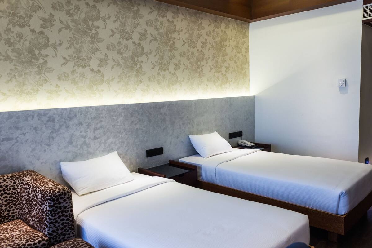 Una habitación de hotel con dos camas individuales, un sillón estampado de leopardo y una pared con estampado floral.