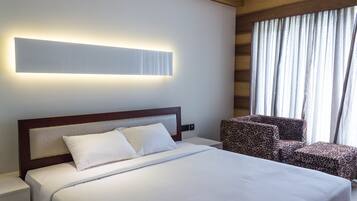 Una habitación de hotel con una cama grande, una mesita de noche, una silla tapizada con estampado de leopardo y una ventana con cortinas.
