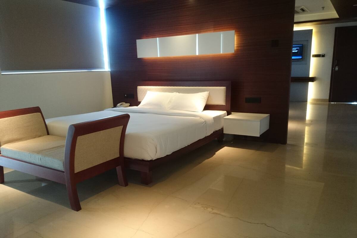 Una habitación de hotel moderna con una cama, mesitas de noche, una silla y un espejo grande.