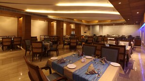 Uma sala de jantar com várias mesas preparadas para o serviço, com uma área de cozinha central.