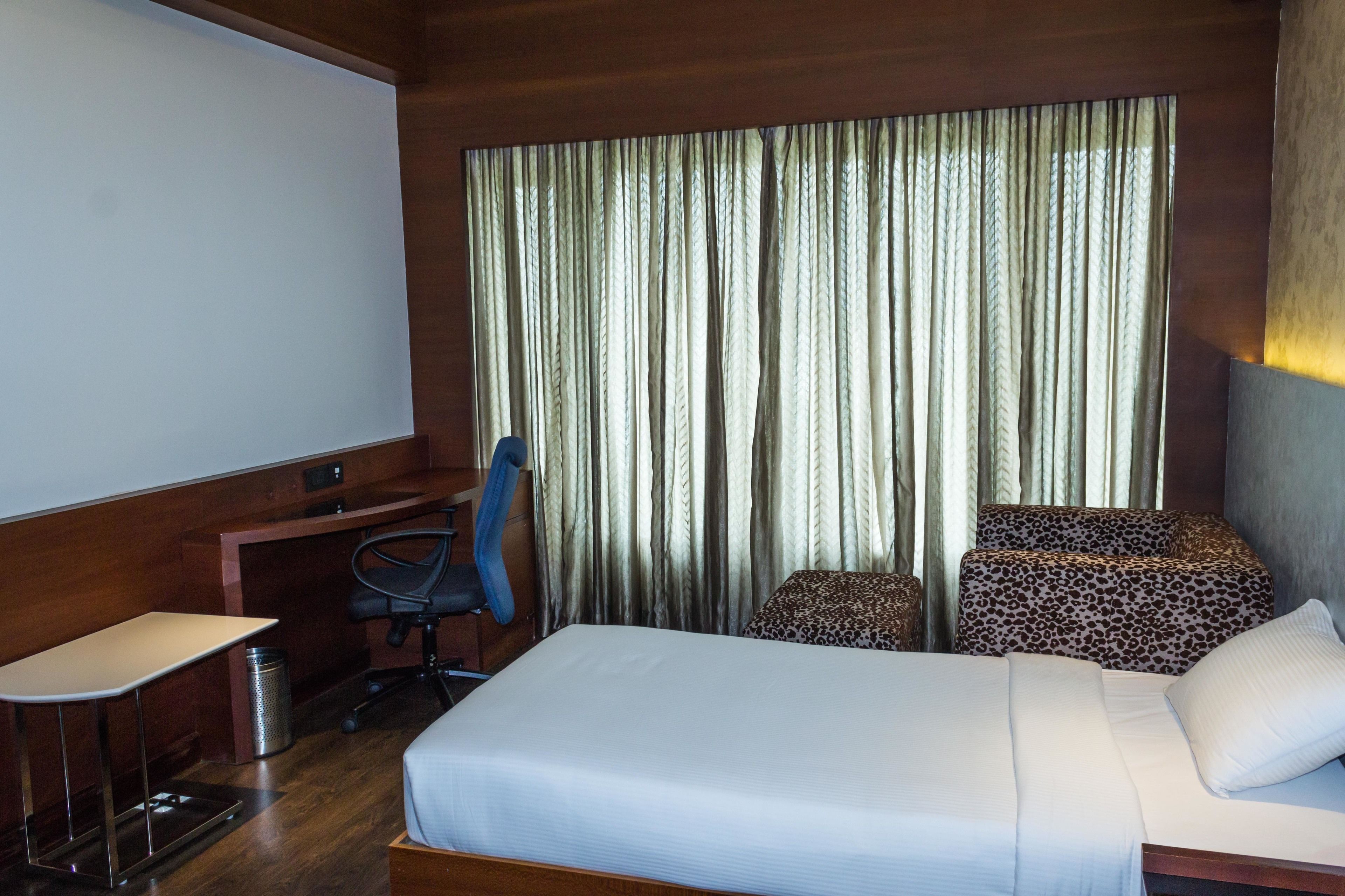 Una camera d'albergo con un letto, una scrivania, una sedia e un'ampia finestra con tende.