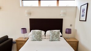 Een net opgemaakt bed met twee kussens, een houten hoofdbord en twee nachtkastjes met lampen.