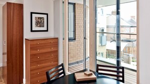 Een moderne kamer met een houten dressoir, een lijst met een foto aan de muur en een balkon met uitzicht op omliggende huizen.
