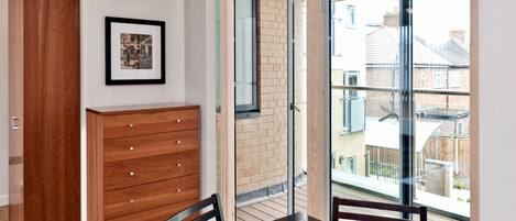 A modern room with a wooden dresser, a framed picture on the wall, and a balcony with a view of neighboring houses.