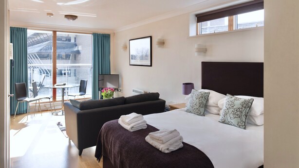 Een moderne hotelkamer met een groot bed, een bank, een zithoek met een tafel en stoelen, en een balkon met uitzicht op de stad.