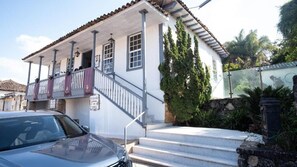 A two-story building with a balcony, steps leading to the entrance, and a car parked in front. - Ville Real Hotel (Ouro Preto)