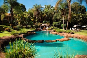 Una piscina con cascada, rodeada de palmeras y follaje.