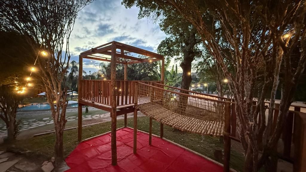 A wooden structure with a platform and a netted area, surrounded by trees and a red mat on the ground.