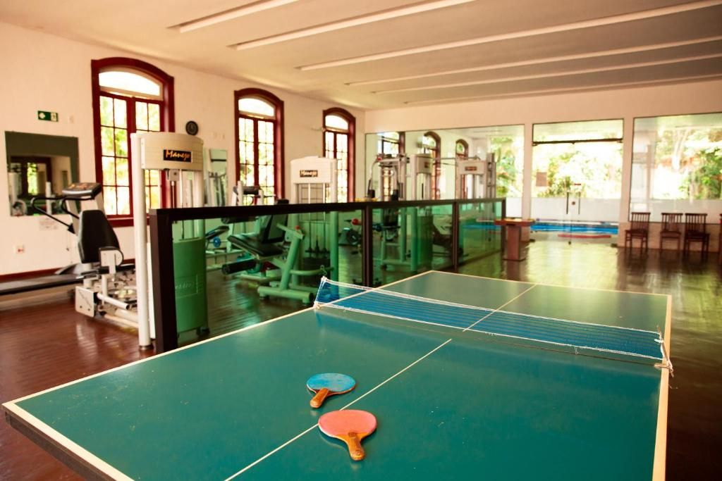 A room with a ping pong table, exercise equipment, and large windows.