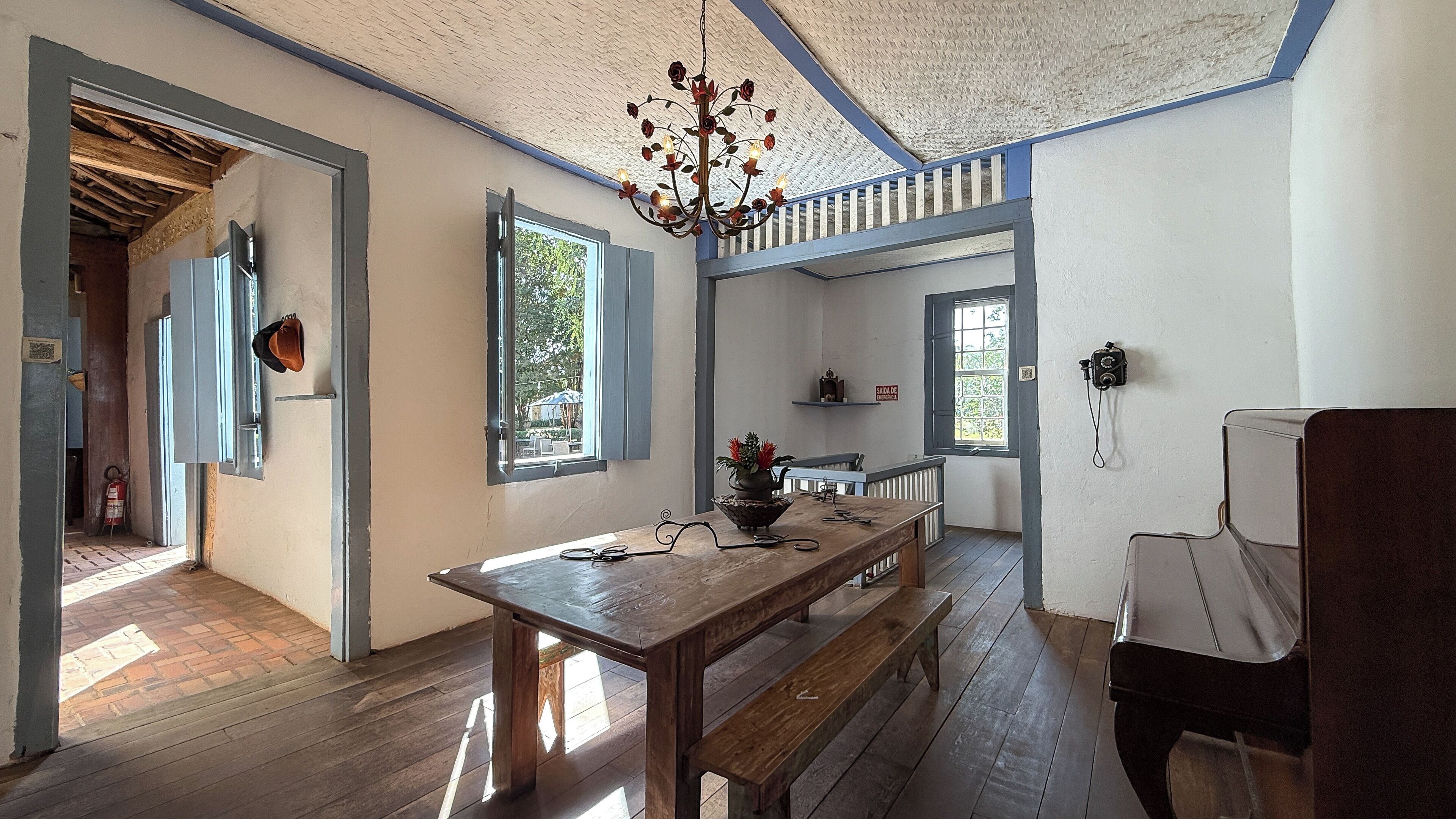 Una habitación con una mesa de madera, bancos, una araña y vistas al exterior.