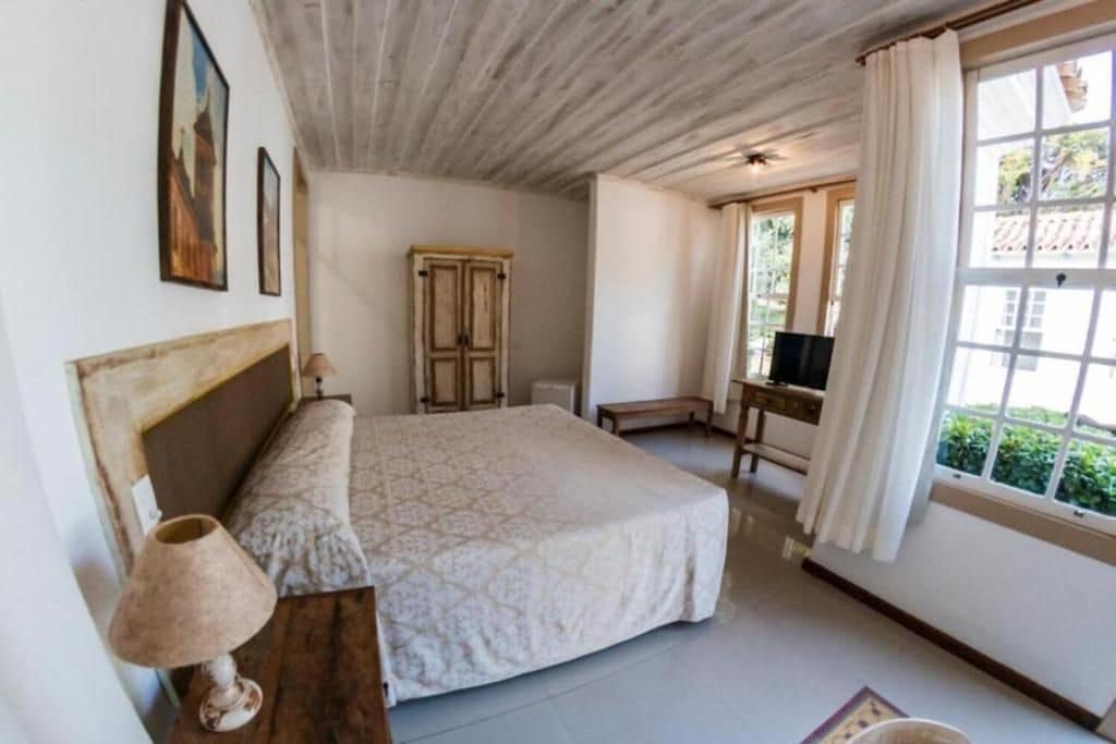 A bedroom with a bed, a desk, a chair, a lamp, and a window with curtains.