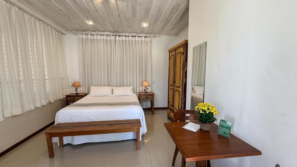 A hotel room with a bed, bedside tables, a wooden bench, a table with a vase of flowers, and a mirror on the wall.