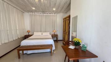 A hotel room with a bed, bedside tables, a wooden bench, a table with a vase of flowers, and a mirror on the wall.