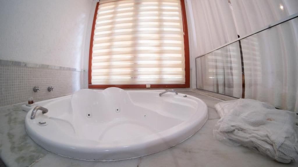 Un baño con una bañera grande, cabina de ducha de vidrio y ventana con persianas.