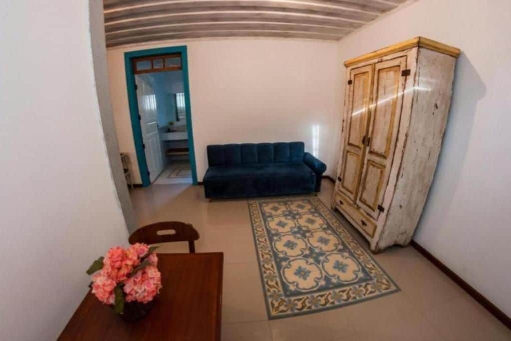 Una habitación con sofá, un armario, un tapete estampado y una mesa con un jarrón de flores.