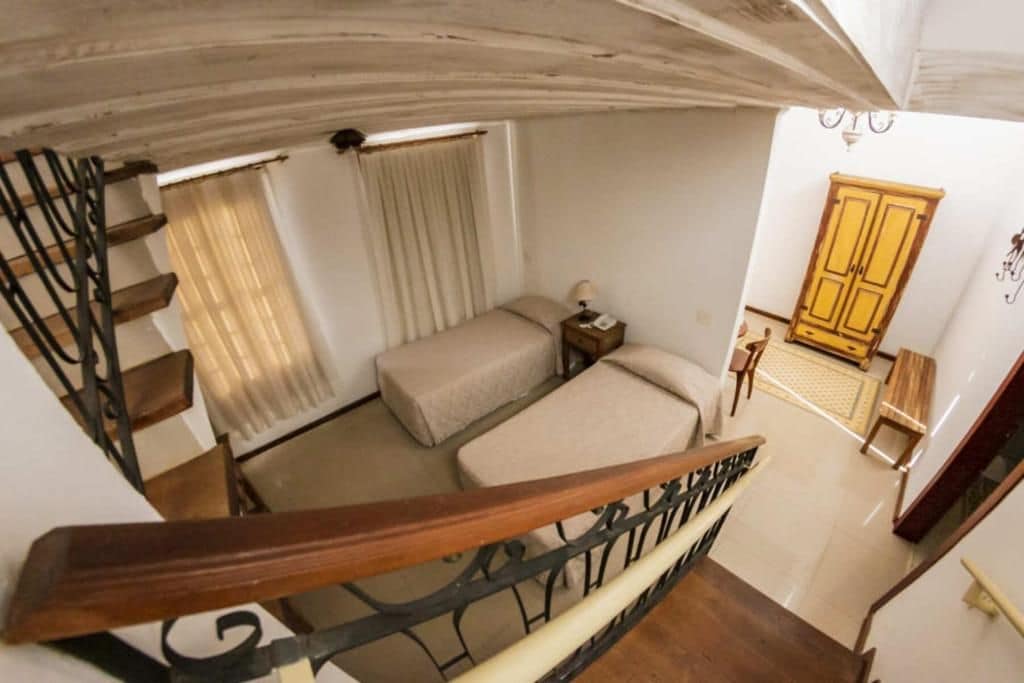 Un dormitorio con cama, mesita de noche, ventana con cortinas, armario de madera y escalera con barandilla de madera.