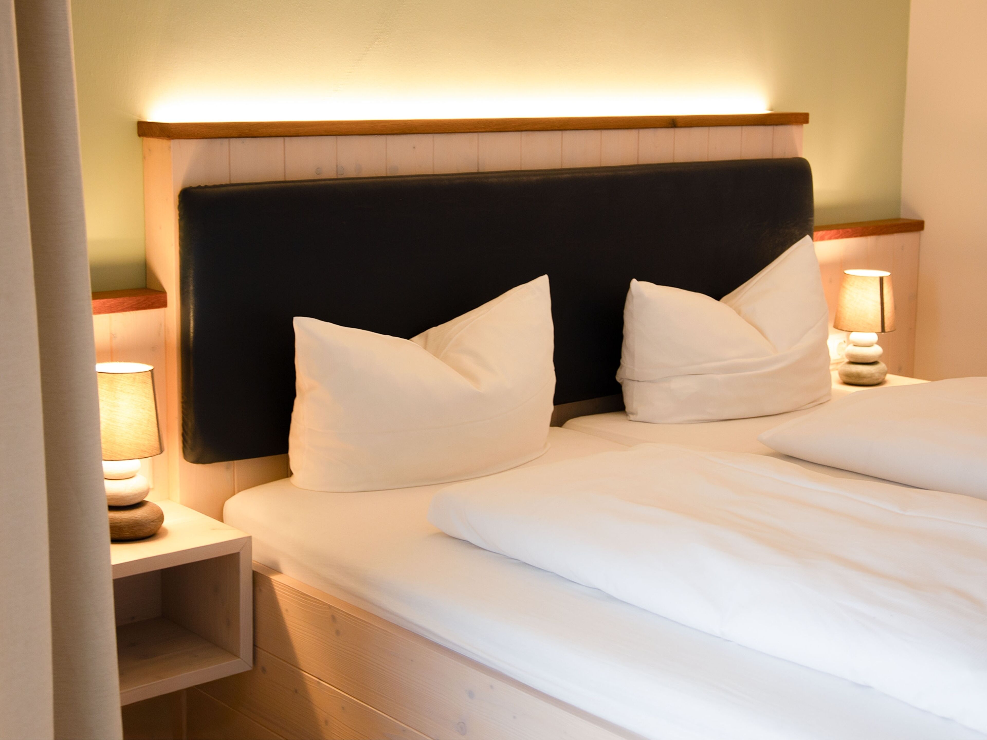 A neatly made bed with white linens and pillows, a wooden headboard, and bedside lamps on a nightstand.