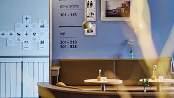 A hotel lobby with a blue wall featuring directional signs for amenities like the sauna, summer sport, and toilets. There are framed pictures and a small table with a vase.
