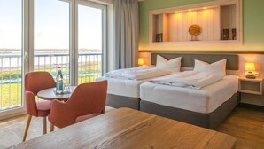 A hotel room with a bed, a table, chairs, a view of the sea, and a wooden headboard. - BE BIO Hotel be natural (Toenning)