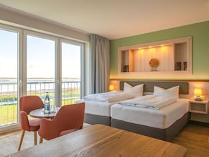 A hotel room with a bed, a table, chairs, a view of the sea, and a wooden headboard. - BE BIO Hotel be natural (Toenning)