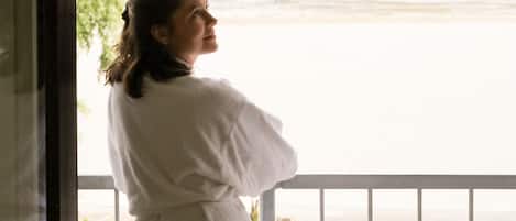 A person in a white robe standing by a window overlooking a river.