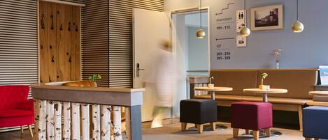 A modern hotel lobby with a reception desk, seating area, and directional signage.