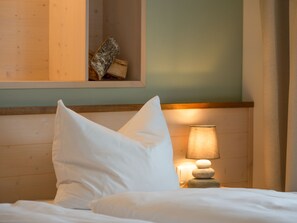 A neatly made bed with white linens, a wooden headboard, a bedside lamp, and a small stack of stones.