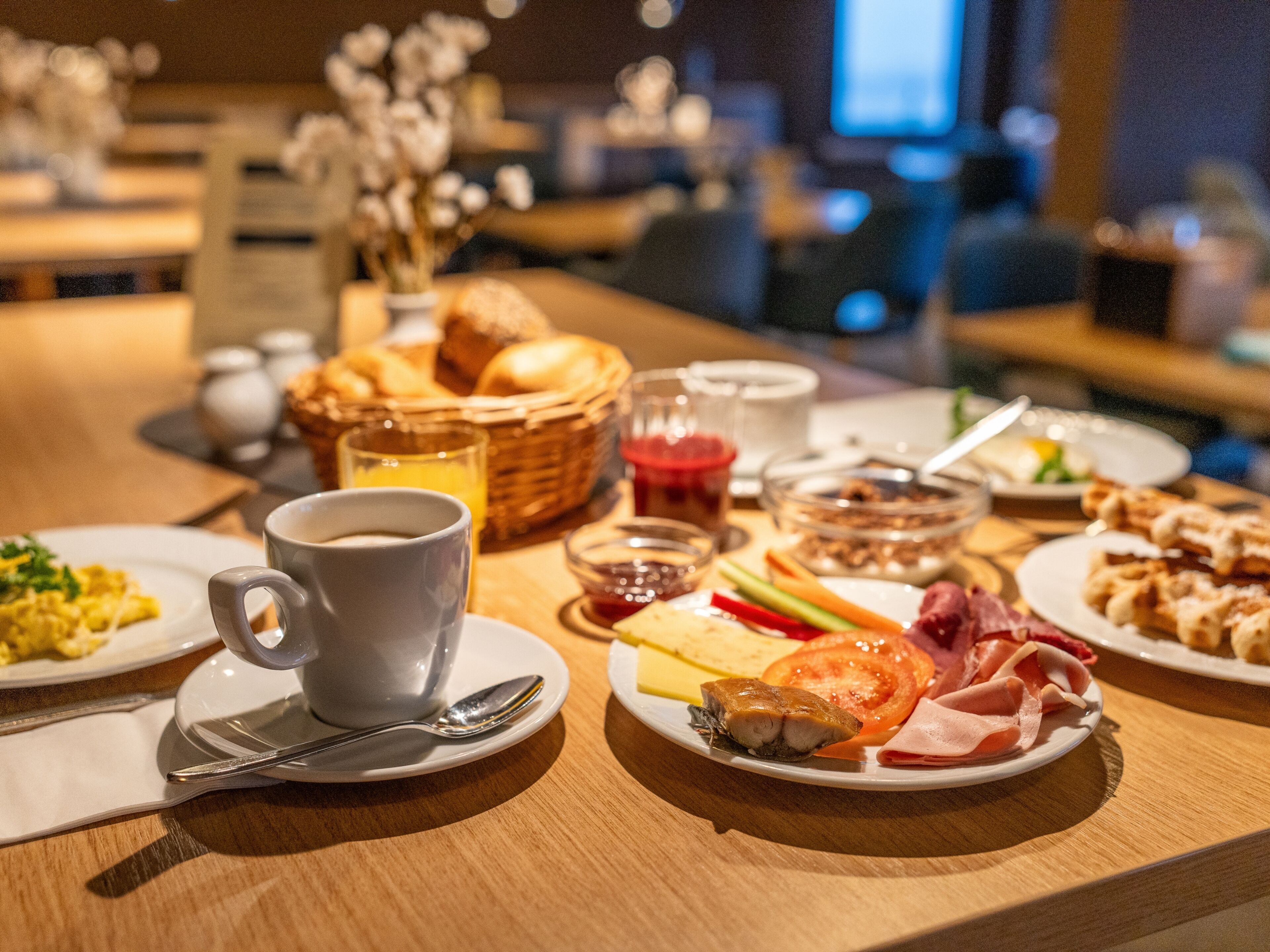 A breakfast setting with plates of food, a cup of coffee, and a basket of bread.