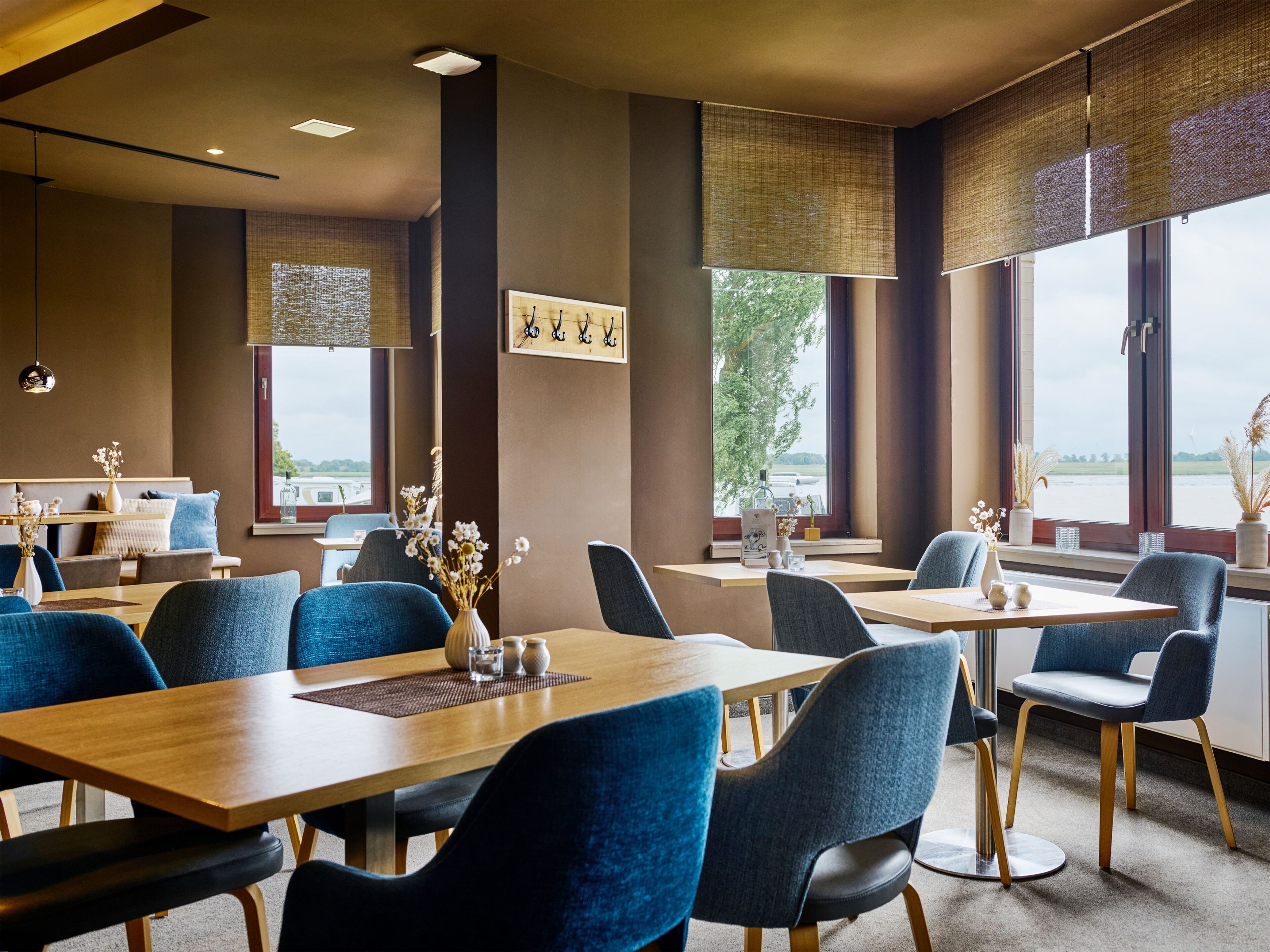 A modern restaurant with high ceilings, large windows, and blue upholstered chairs.