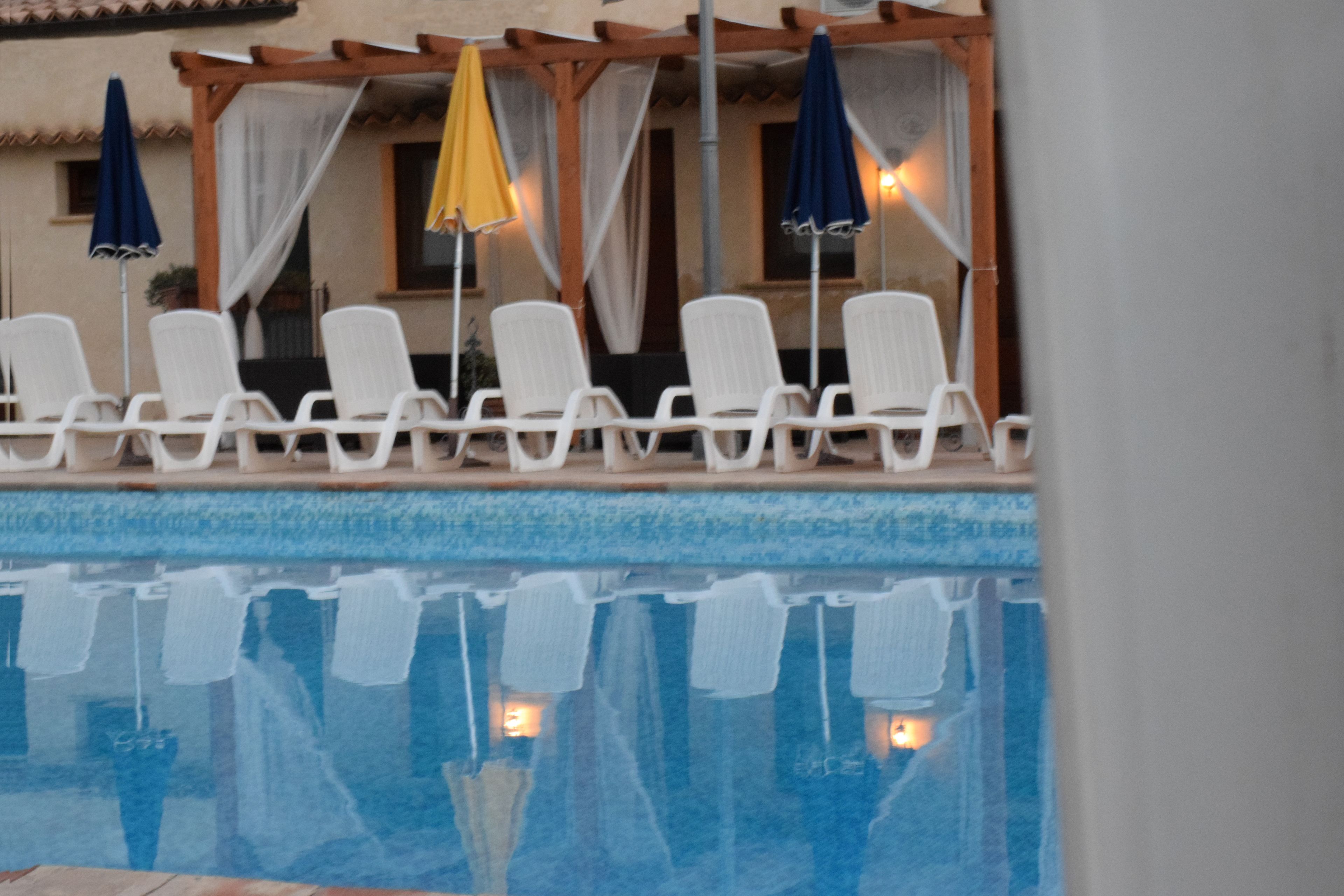 Un área junto a la piscina con sillas reclinables blancas y sombrillas.