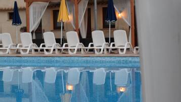 Un área junto a la piscina con sillas reclinables blancas y sombrillas.