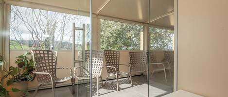 A modern room with large windows, metal chairs, a white table, and a potted plant.