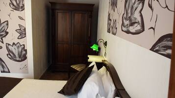 Una camera d'albergo con un letto, un comodino, una lampada, una sedia e un armadio.