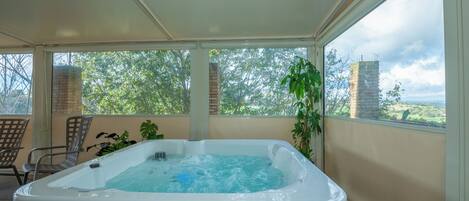 A hot tub in a covered outdoor area with a view of trees and a brick chimney.