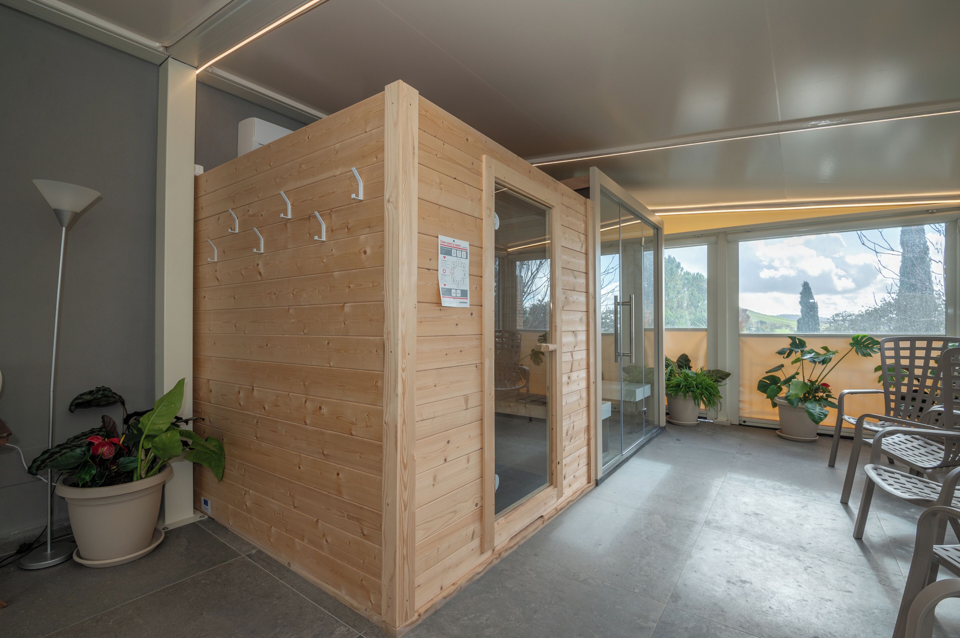 A wooden sauna with glass doors, potted plants, and a balcony with chairs.