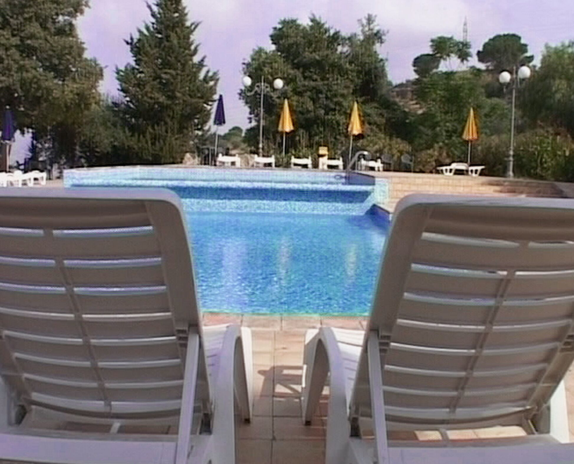 A swimming pool with lounge chairs facing the water, surrounded by trees and umbrellas.