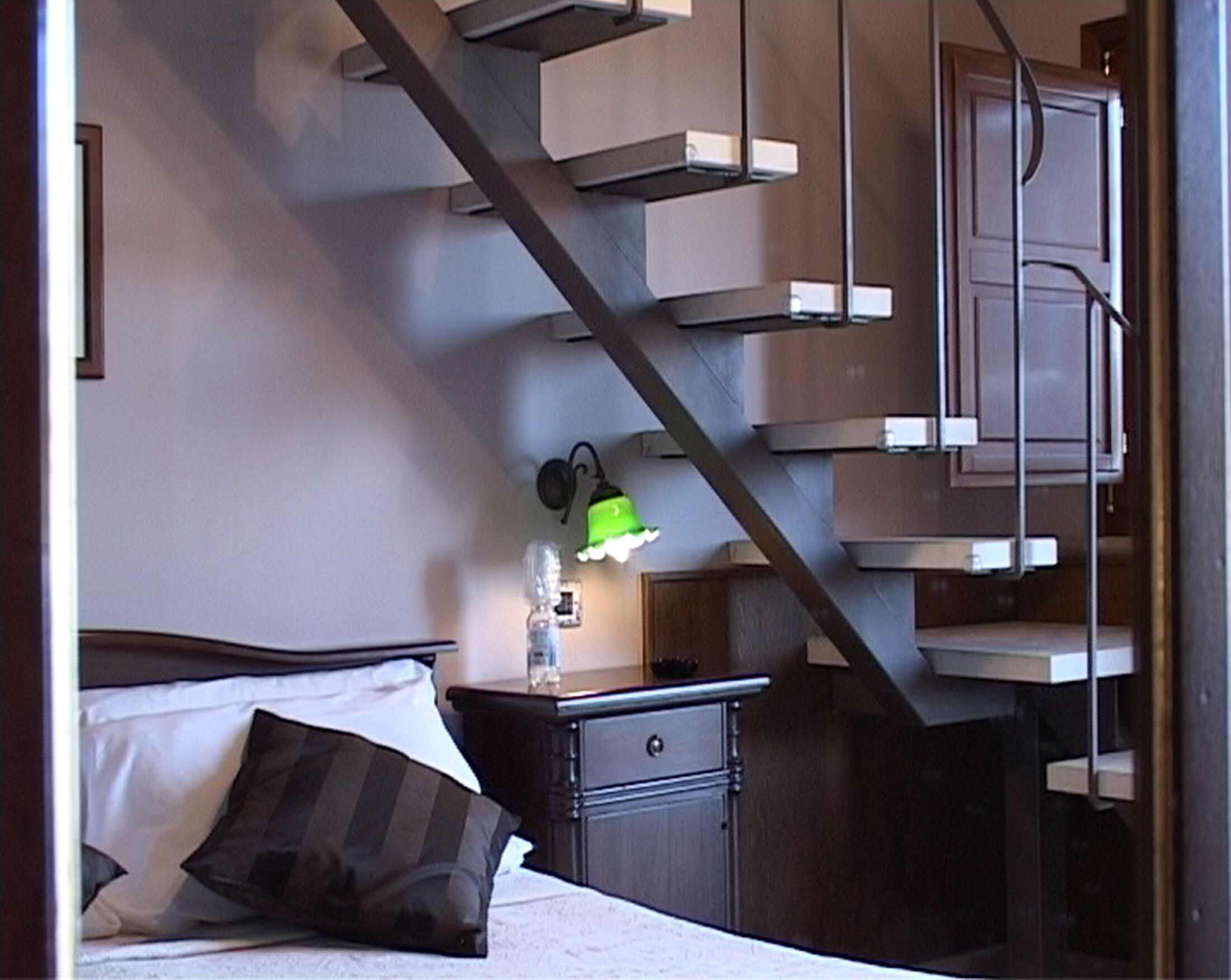 A bedroom with a bed, a nightstand, a dresser, and a staircase.