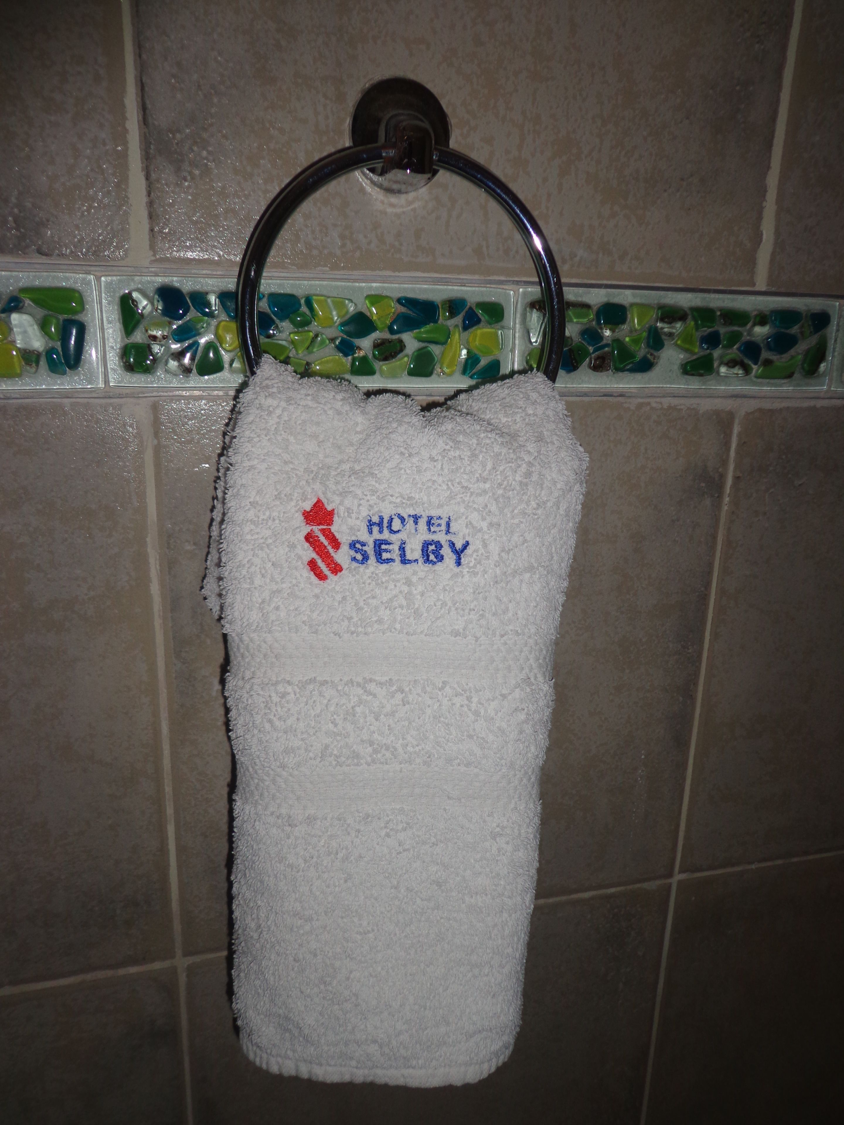 A white towel hanging on a metal ring, with the text "HOTEL SELBY" embroidered on it.