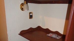 Un rincón de una habitación con una estantería de madera, un escalón pequeño y una lámpara fijada a la pared.