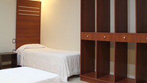 Habitación de hotel con dos camas, un armario de madera y una mesita de noche.