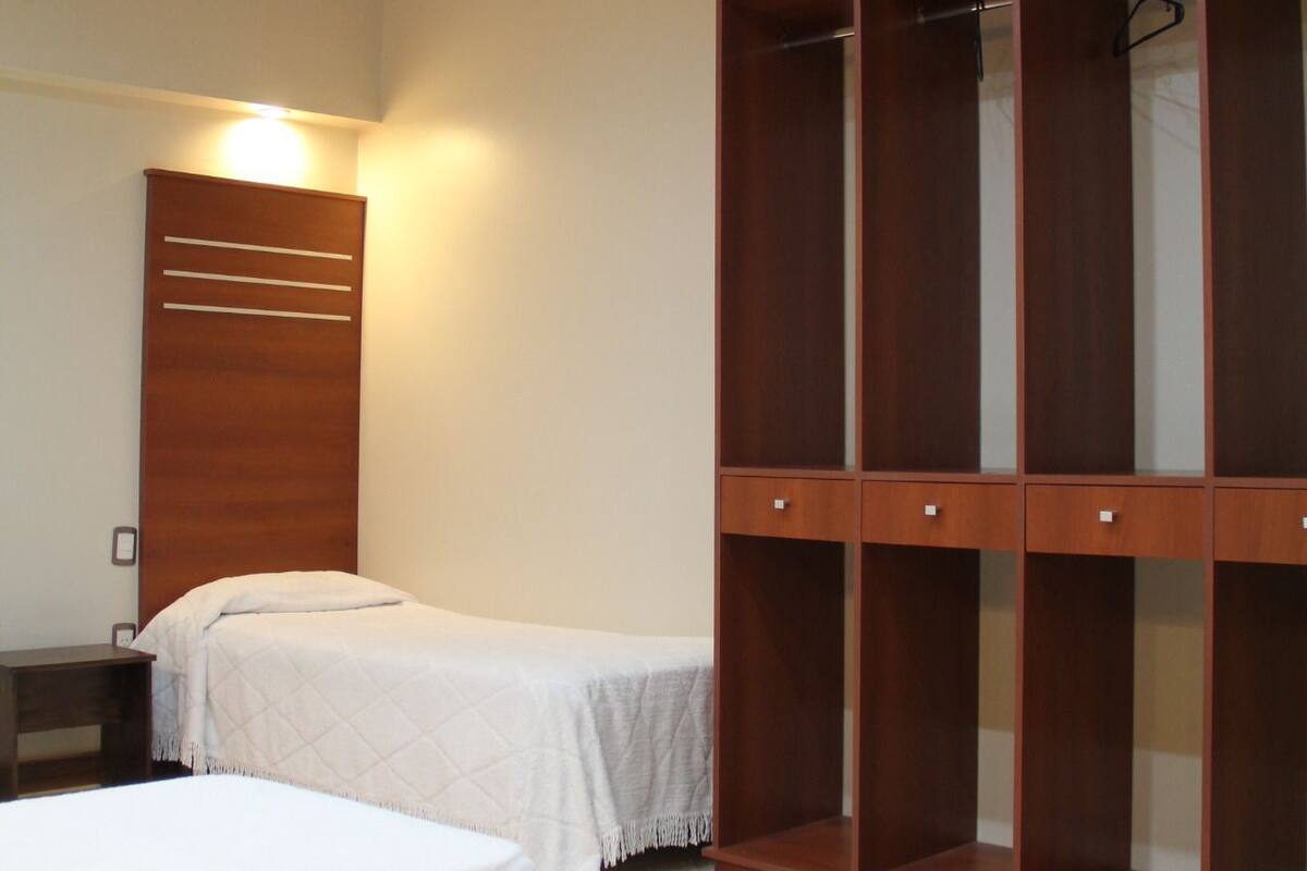 A hotel room with two beds, a wooden wardrobe, and a bedside table.