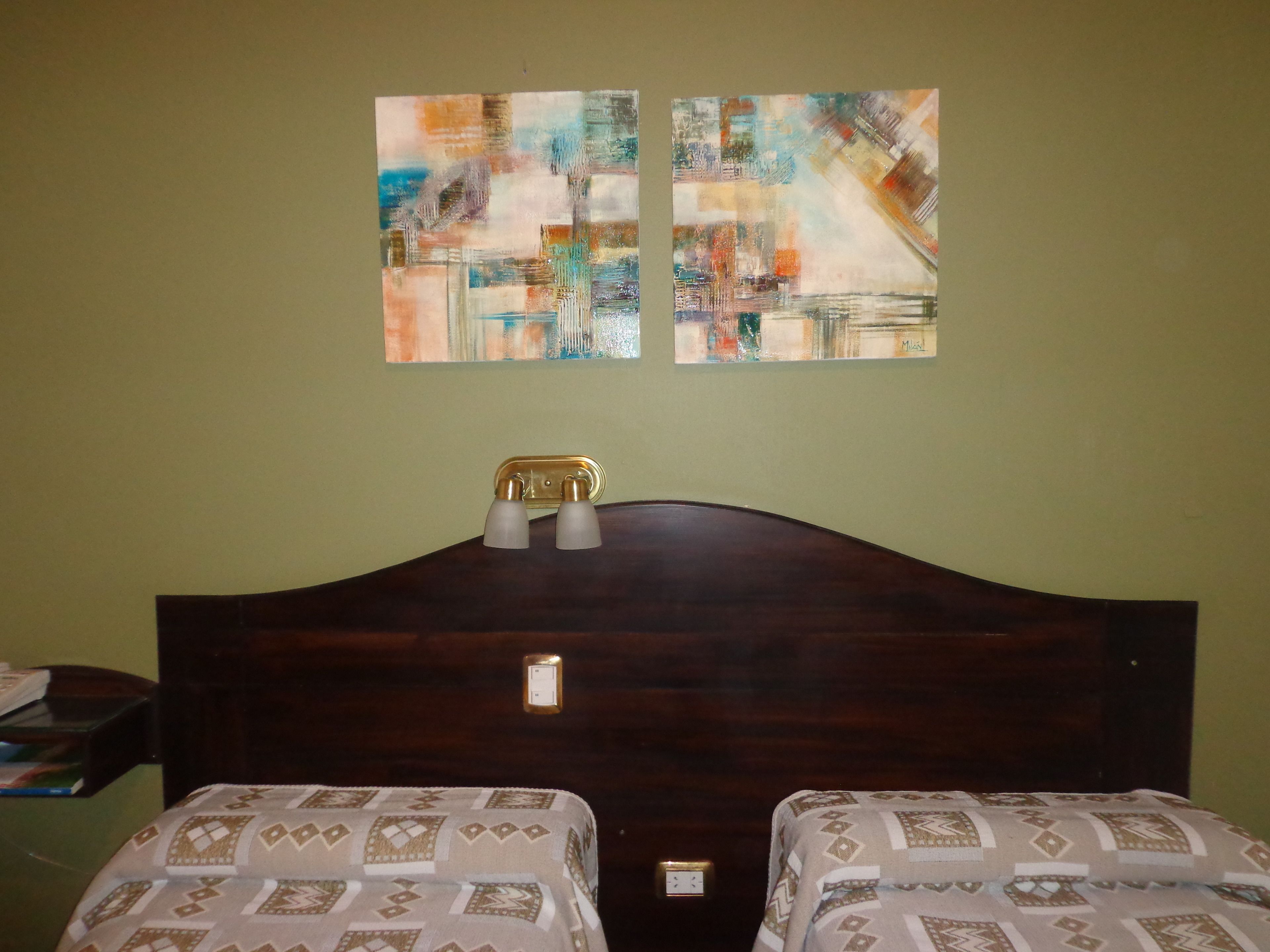 A room with two beds, a wooden headboard, a nightstand, and abstract art on the wall.