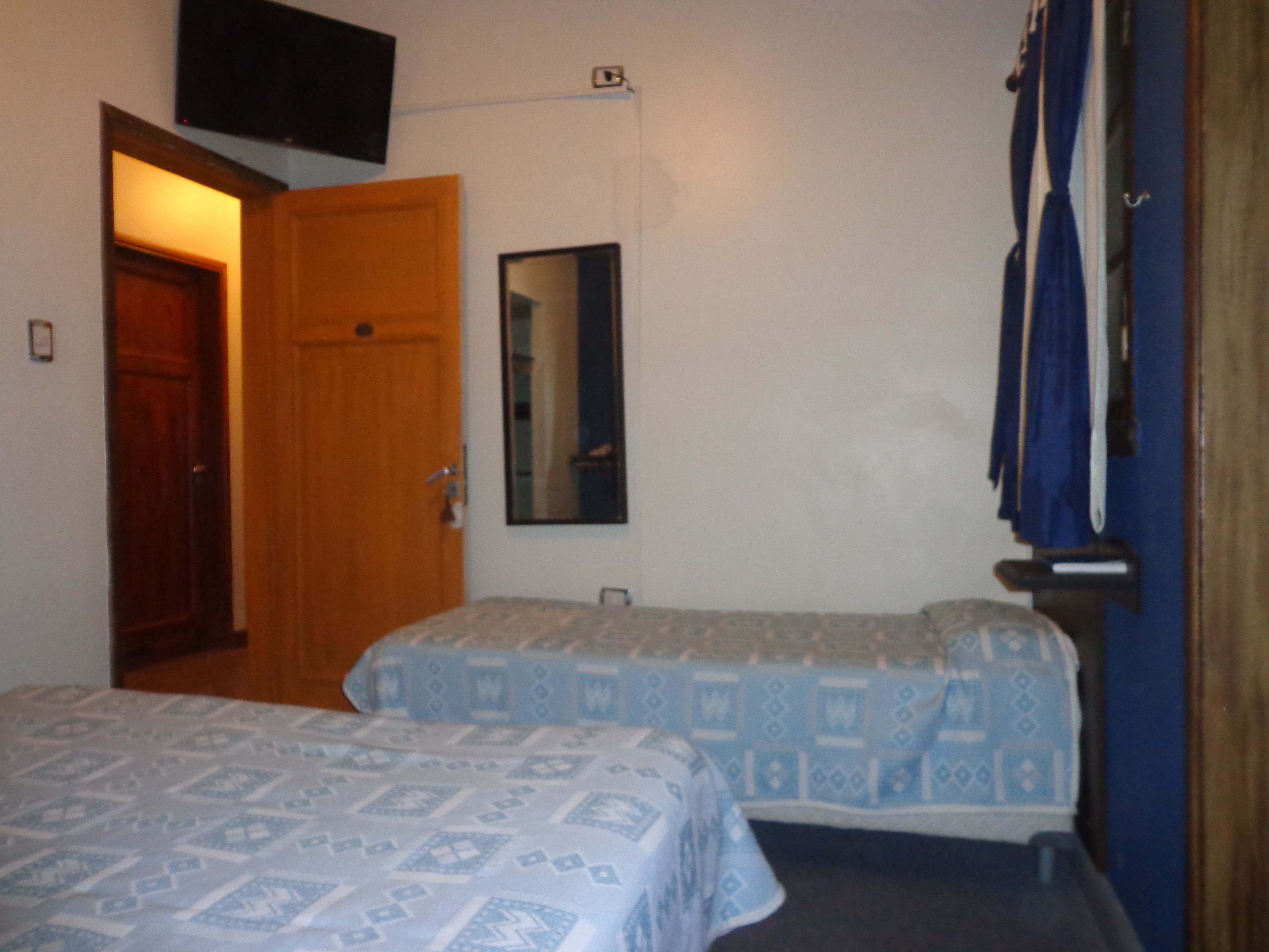 A room with two beds, a wooden door, a mirror, and a television on the wall.