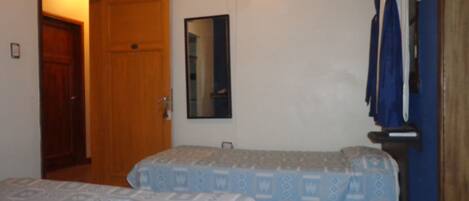 A room with two beds, a wooden door, a mirror, and a television on the wall.