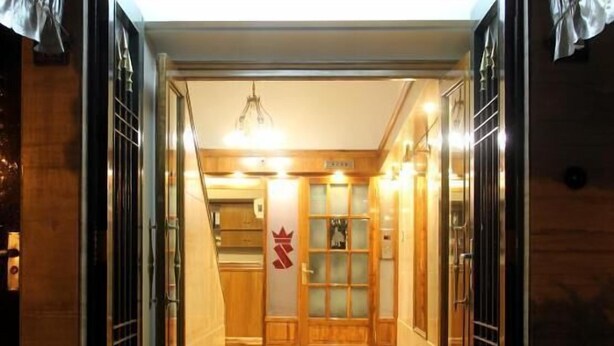 Un vestíbulo de hotel con un mostrador de recepción de madera, una puerta de vidrio con un logo y una araña.