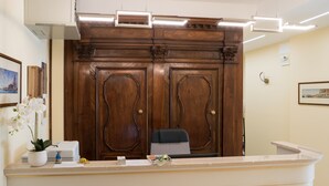 A reception desk with a wooden backdrop, a chair, a potted plant, and a small figurine. - Guest House Train Station (Mestre)