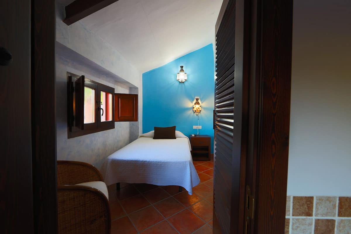 Um quarto com uma cama, uma mesa de cabeceira, uma luminária na parede e uma porta.